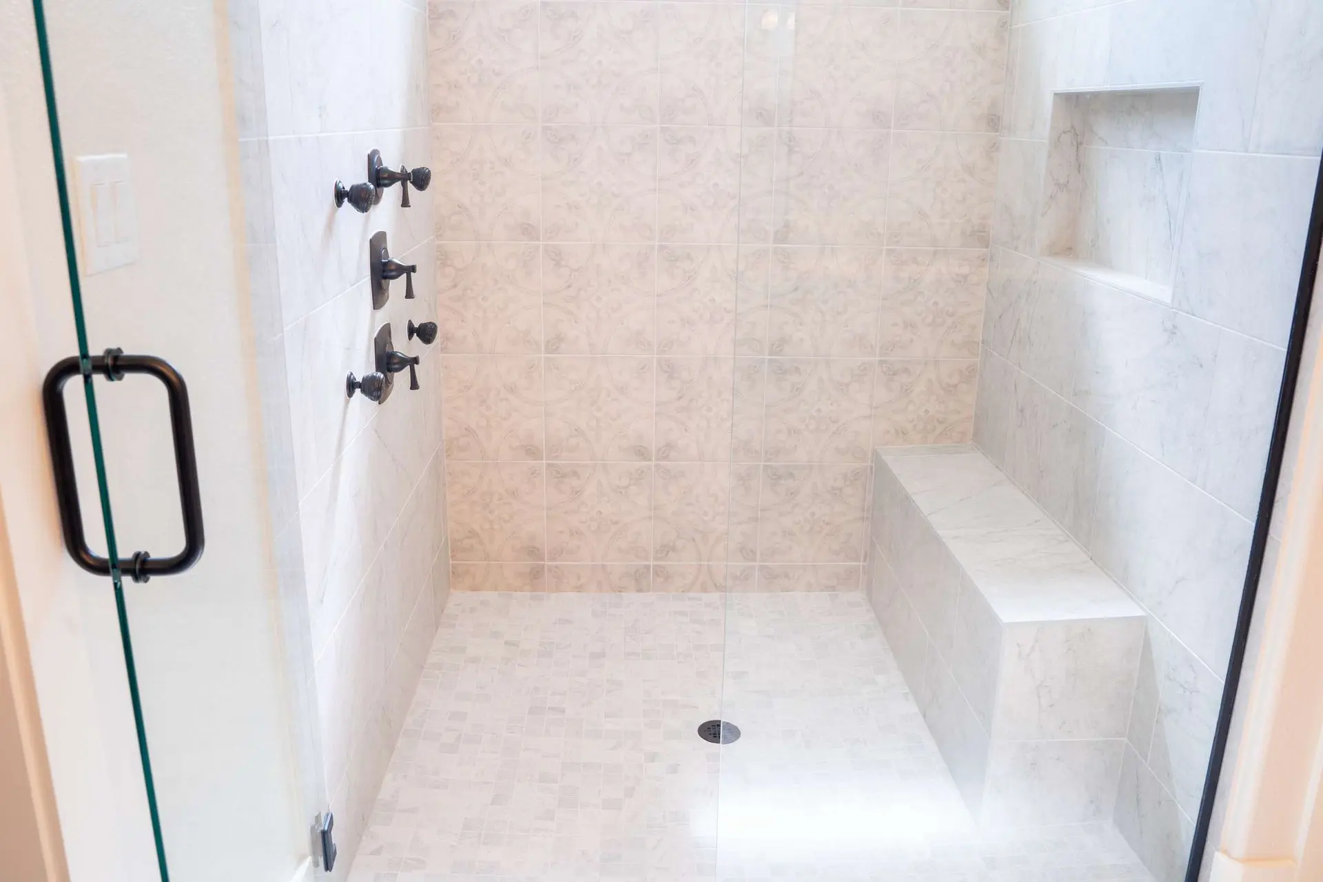 Walk-in shower with decorative medallion tile accent wall built-in bench and glass door in League City TX