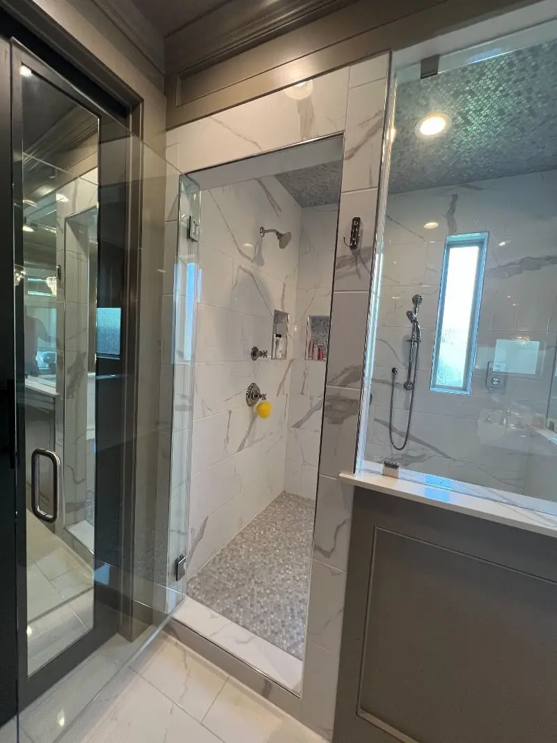 Modern marble walk-in shower with glass enclosure pebble floor and penny tile accent in Friendswood TX