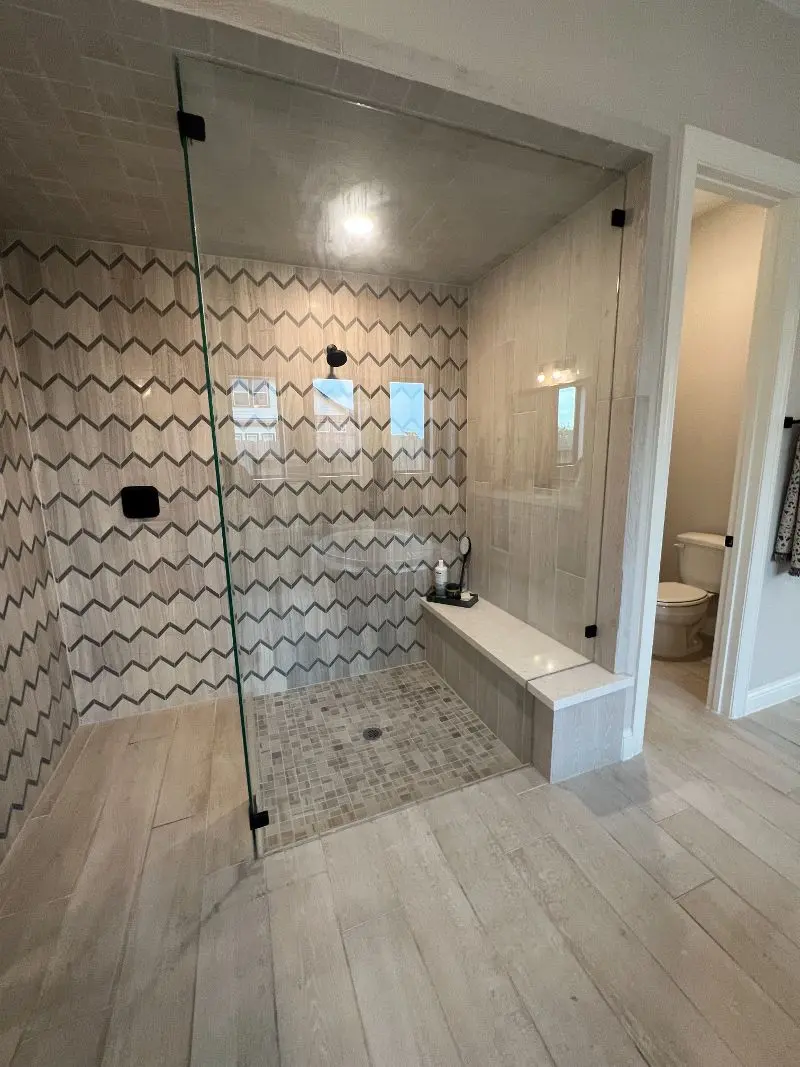 Walk-in shower with chevron tile accent wall built-in bench and frameless glass door in League City TX