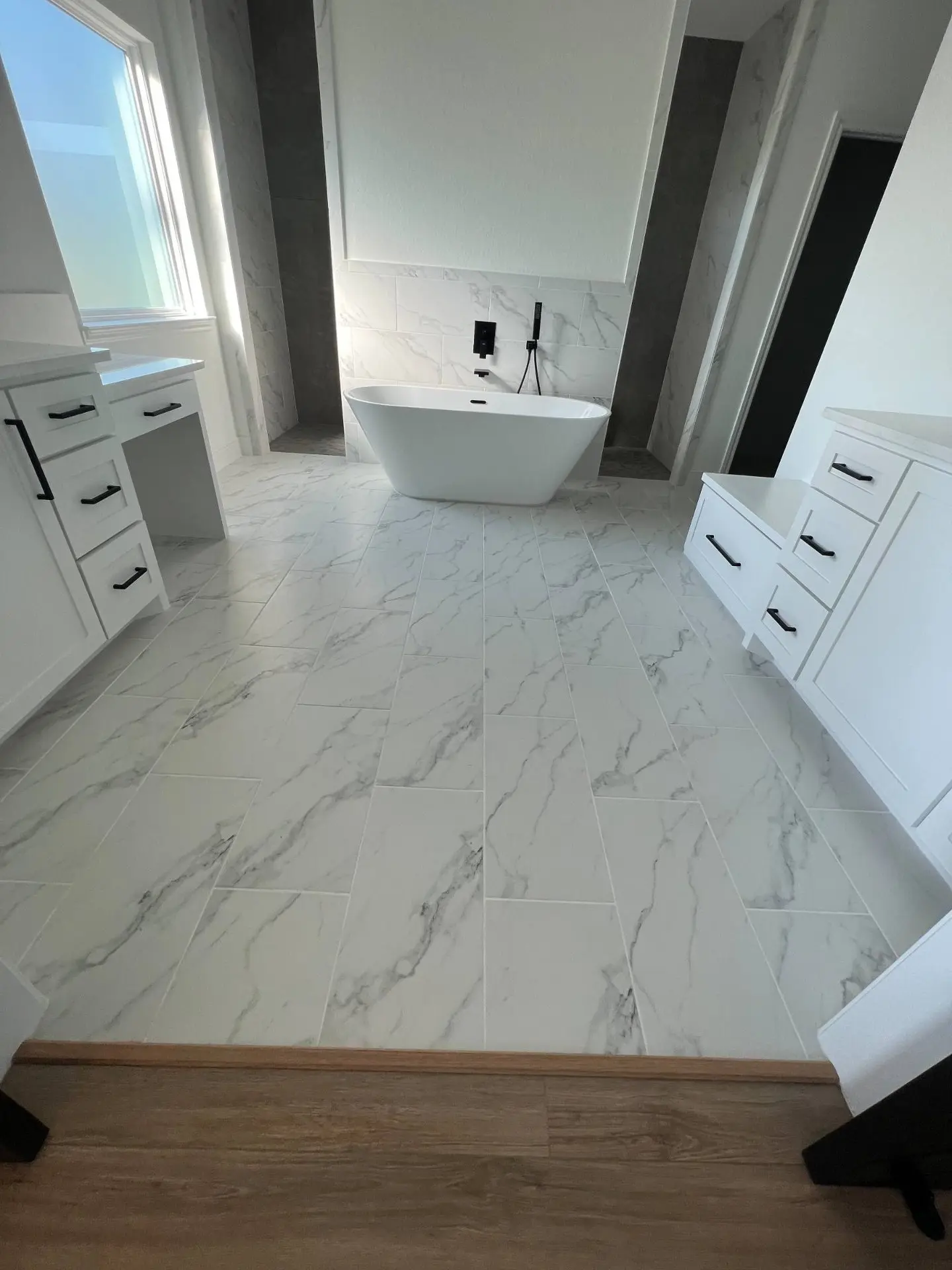 Modern white bathroom with freestanding tub marble look tile and dual white shaker vanities in Dickinson TX