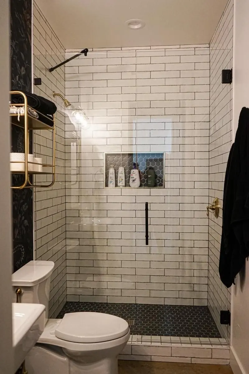 Subway tile shower with black hexagon niche accent brass fixtures and dark wallpaper in Texas City