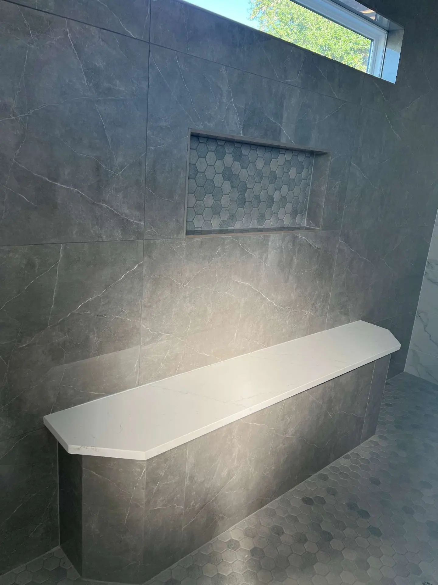 Dark marble shower with quartz bench hexagon niche and modern fixtures in League City TX