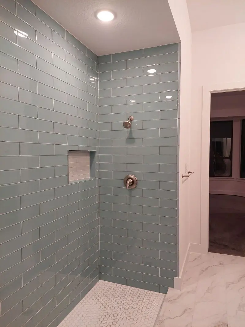 Aqua glass subway tile walk-in shower with hexagon floor and nickel fixtures in Texas City