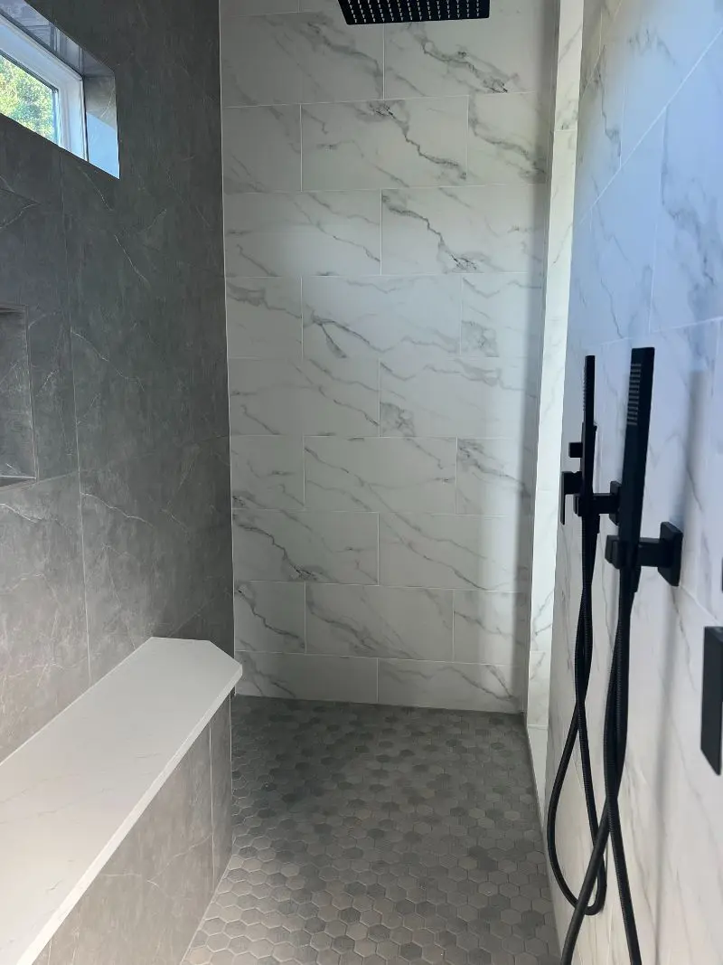 Two-tone marble walk-in shower with black rain head quartz bench and hexagon floor in Manvel TX