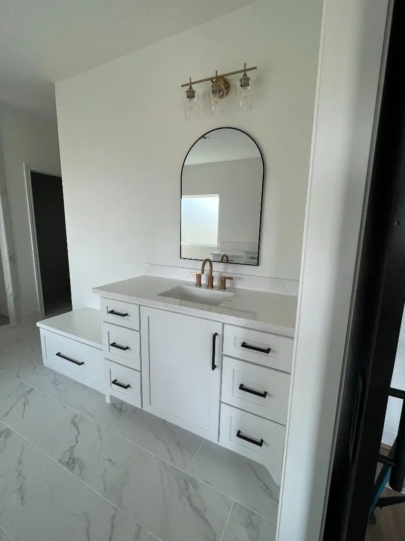 White floating vanity with quartz top arched mirror and brass fixtures in Alvin TX bathroom