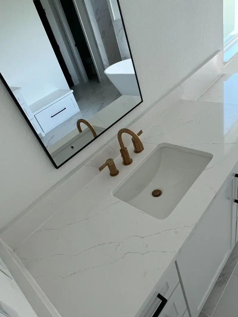 White quartz vanity countertop with brass fixtures and modern black framed mirror in League City TX