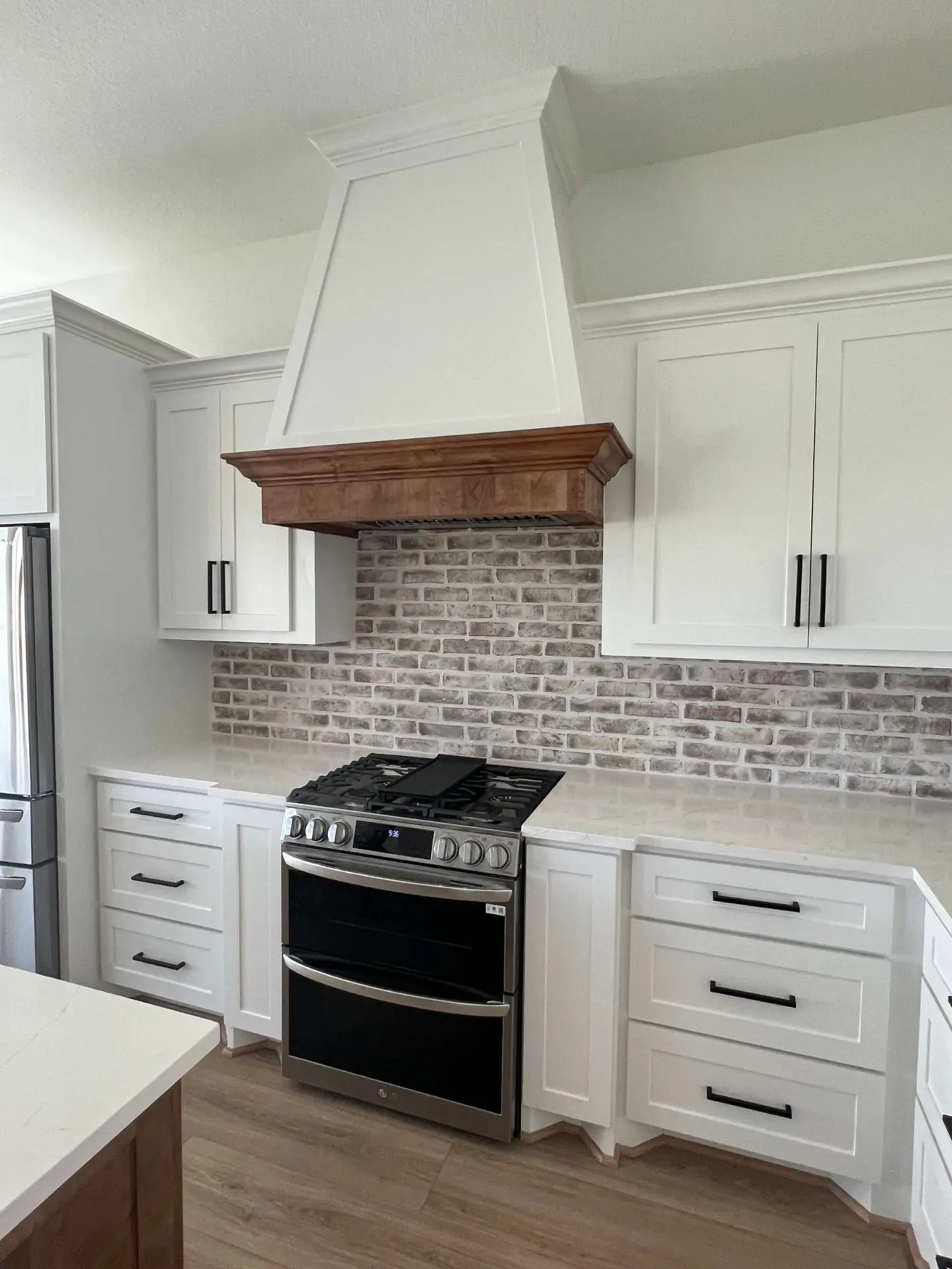 Farmhouse kitchen with white shaker cabinets brick backsplash and custom wood range hood in Pearland TX