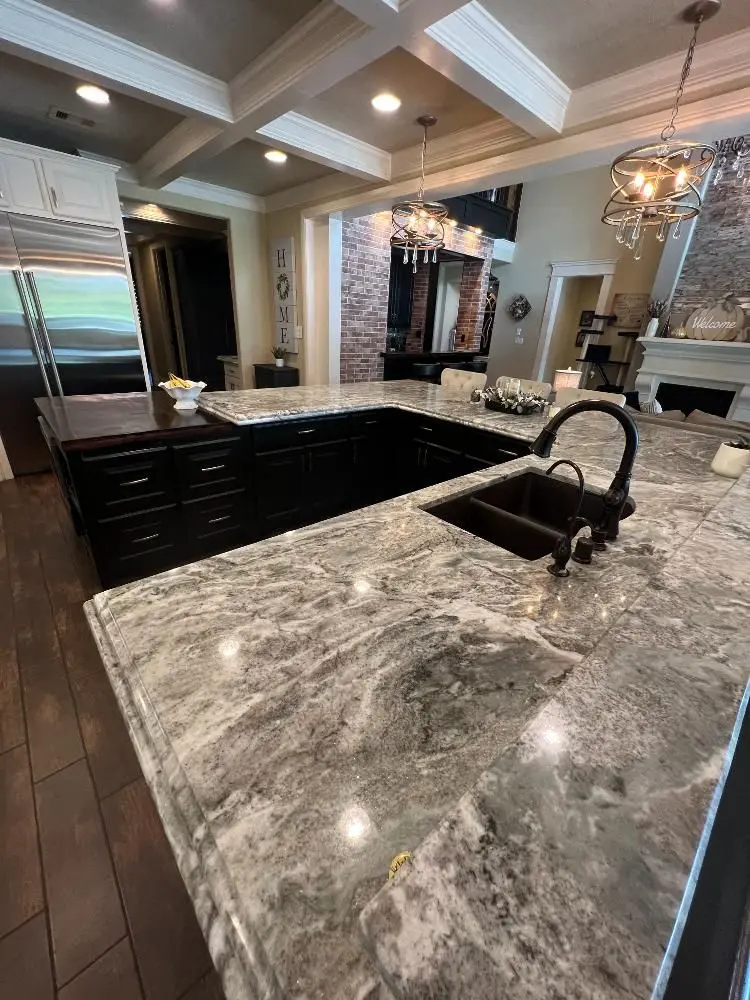 Large gray granite kitchen island with dark cabinets and modern fixtures in Friendswood TX