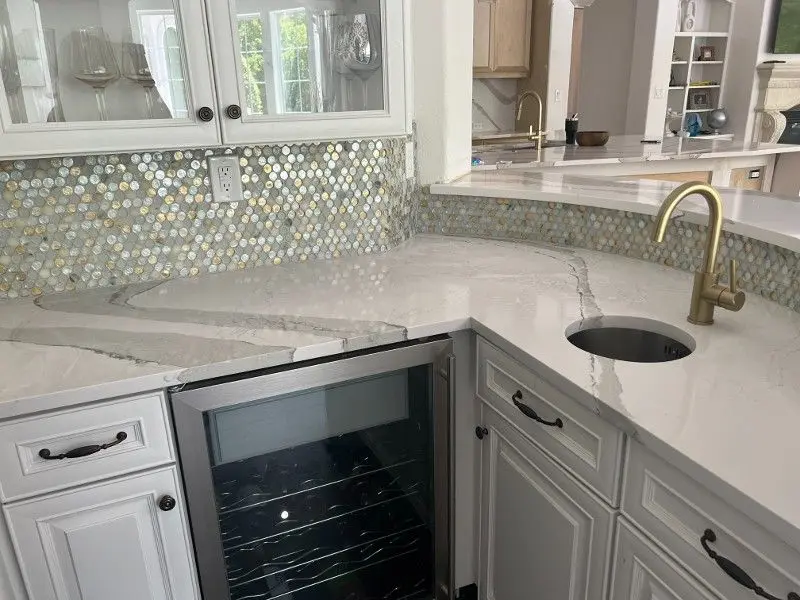 Quartzite wet bar with penny tile backsplash brass fixtures and wine cooler in League City TX