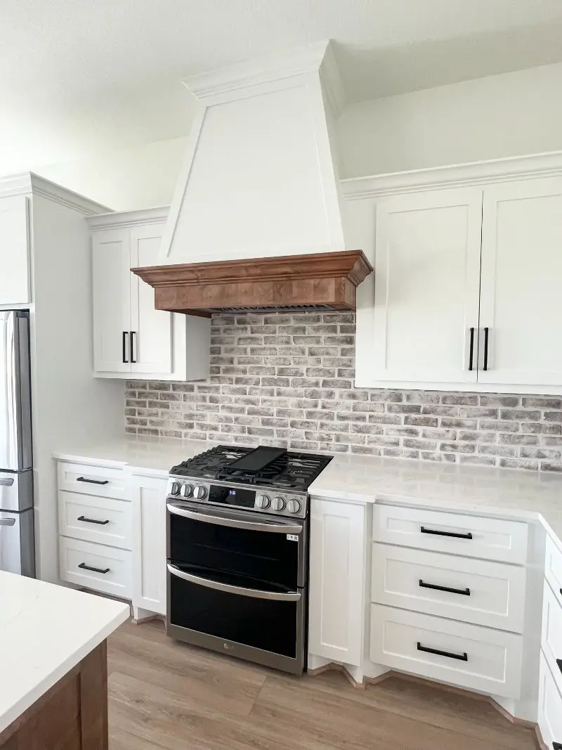 Modern farmhouse kitchen with white cabinets brick backsplash and wood range hood trim in Friendswood TX