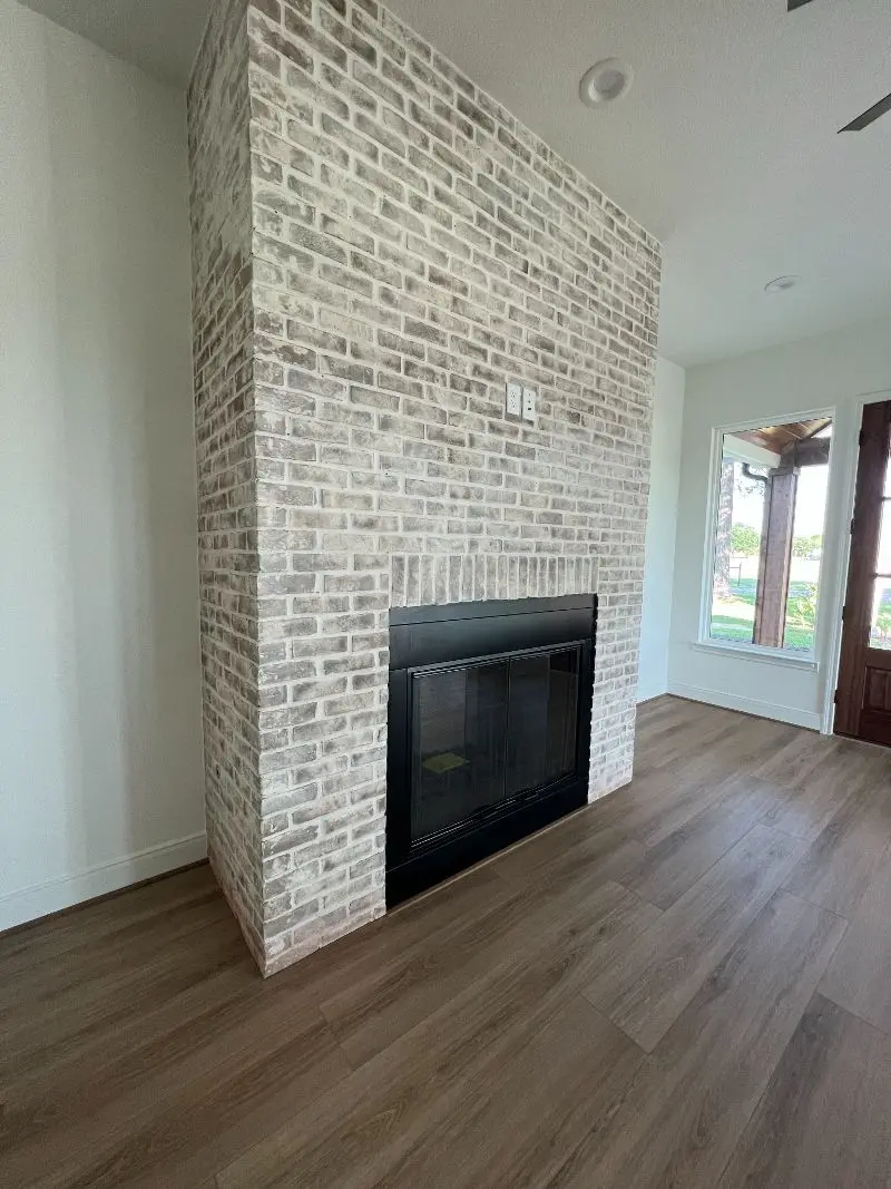 Floor-to-ceiling whitewashed brick fireplace with black insert and wood plank floors in Texas City